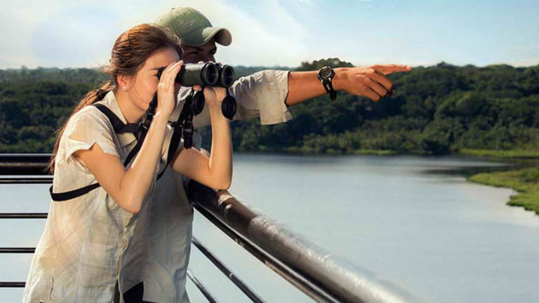 A traveler looks through binoculars while another traveler points, near the Napo Wildlife Center, a sustainable eco lodge surrounded by a 53,000 acre rainforest biosphere reserve within Yasuni National Park in the Amazon.