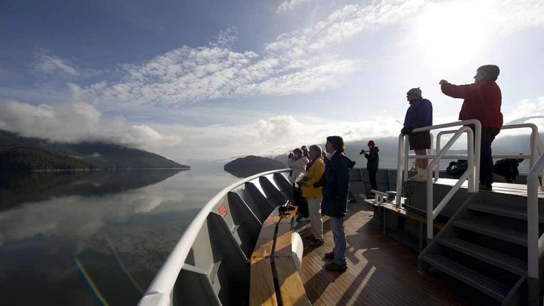 Alaska travelers stand out on deck near ship's bow on a sunny day of the Exploring Alaska's Coastal Wilderness cruise.