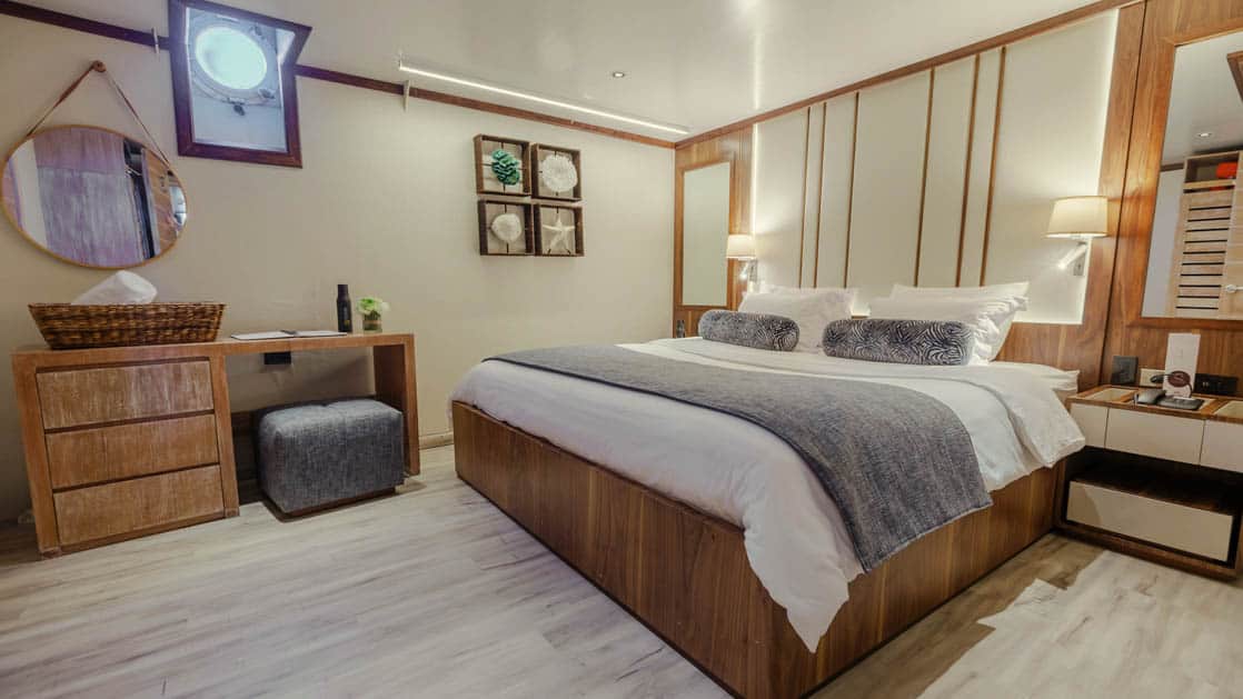Evolution deluxe stateroom with king bed, dresser with desk and porthole.