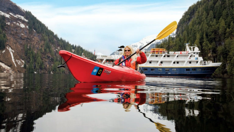 The Lindblad Expeditions ships cruising in Southeast Alaska with a kayaker paddling in front