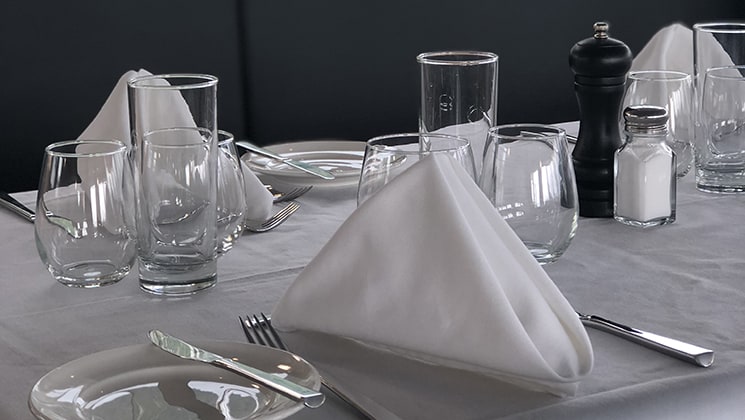 Dinner table set up with wine glasses, silverware, grey tablecloth & white napkins, on the Kruzof Explorer Alaska small ship.