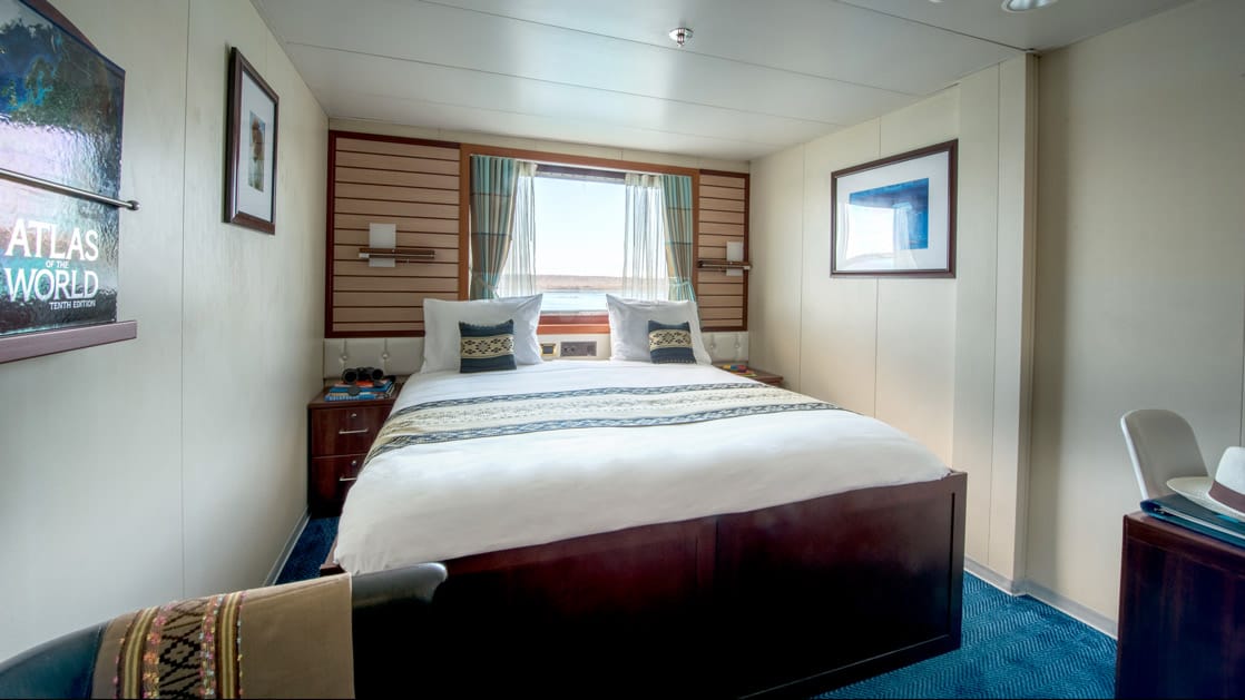Cabin with large bed, armchair, large window aboard National Geographic Endeavour II in the Galapagos Islands