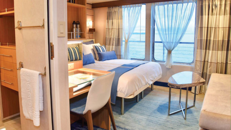 Category 5 suite with large bed, sofa, coffee table, desk, chair and large windows aboard National Geographic Quest luxury expedition ship