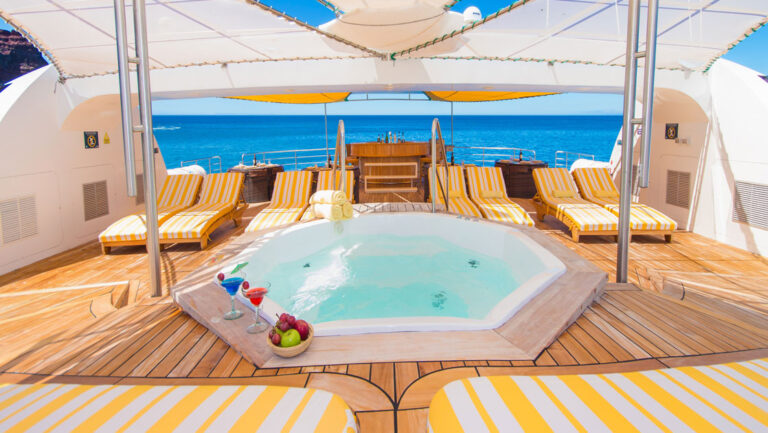 Empty Jacuzzi amongst teak decking & yellow-&-white-striped chaise lounges on sun deck of Petrel boat in Galapagos.