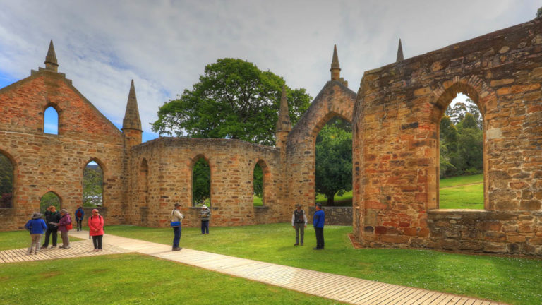people stand on the grass in front of the stone walls of port arthur in australia on a cloudy day