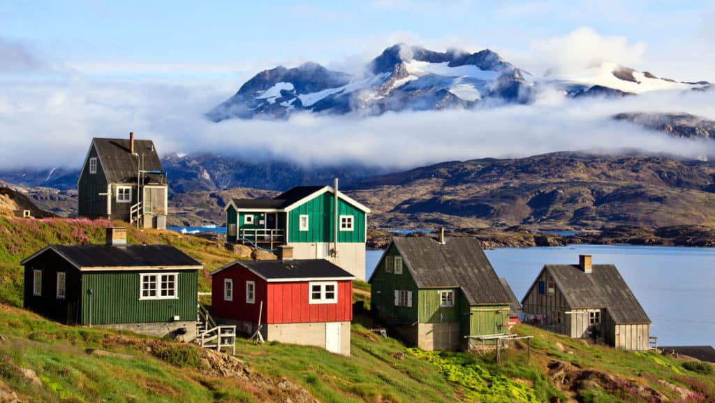 a group of small colorful houses on a hillside in greenland with the sea and large mountains in the background