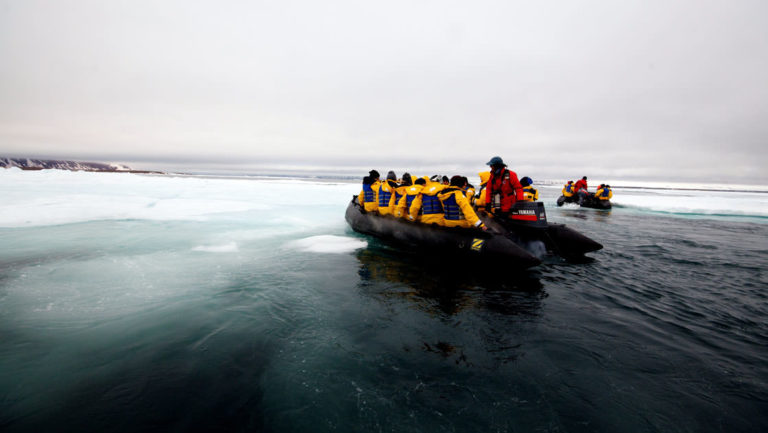 adventure travelers on the three arctic islands iceland, greenland, spitsbergen small ship cruise take a zodiac over calm waters with ice underneath
