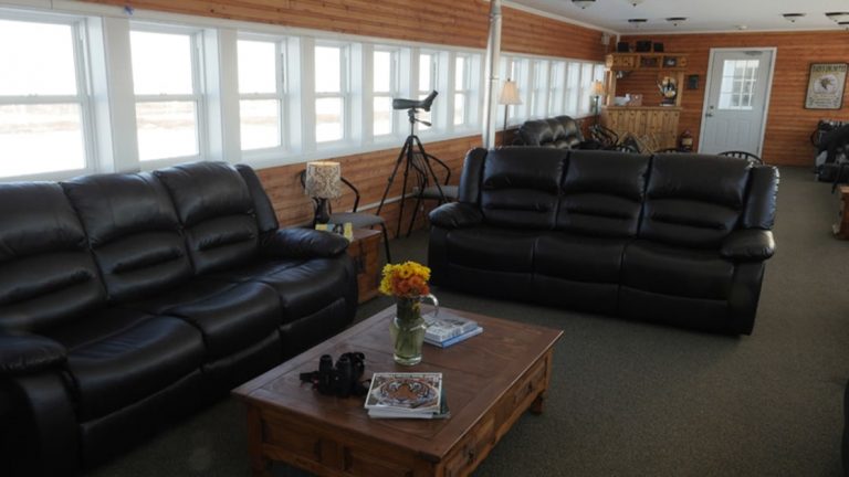 Two leather sofas, binoculars and a coffee table in the Tundra Lodge lounge with windows overlooking the Canadian Arctic.