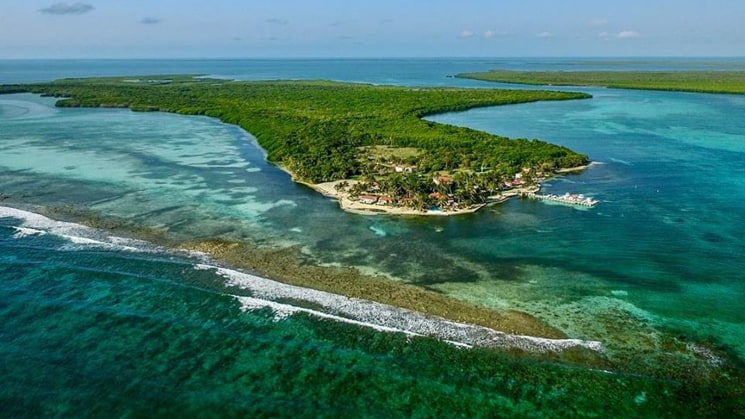 A overhead view of Turneffe Flats Lodge with trees, island and blue water.