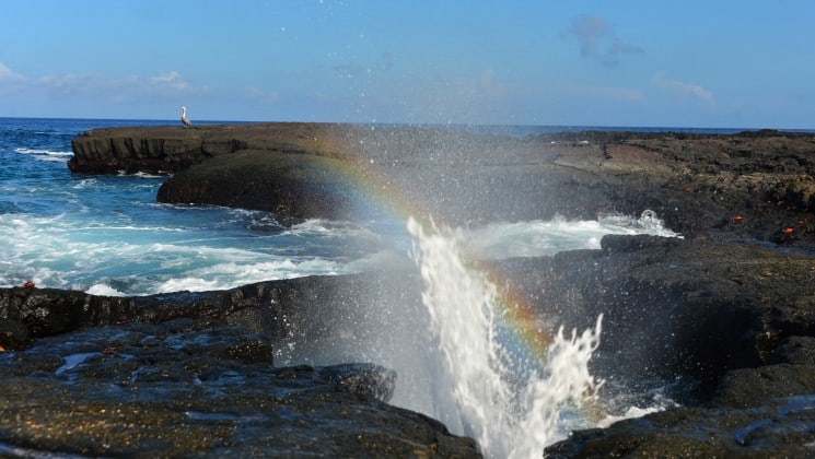 spray from a wave crashes between rocks creating a rainbow at the galapagos islands