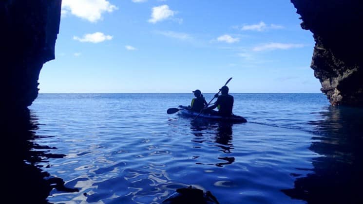A kayak paddles on blue water between two silhouetted rocks at the galapagos islands