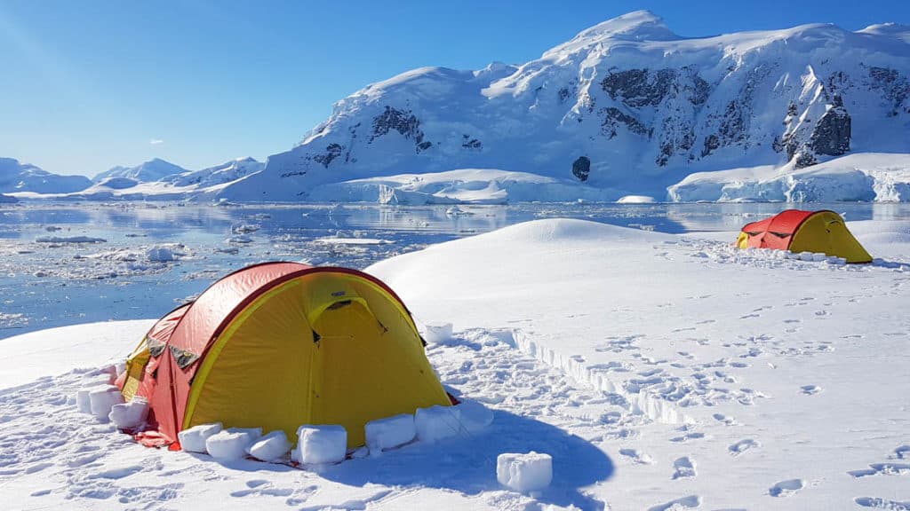 yellow and orange tent set up on the snow in antarctica with a large mountain in the distance