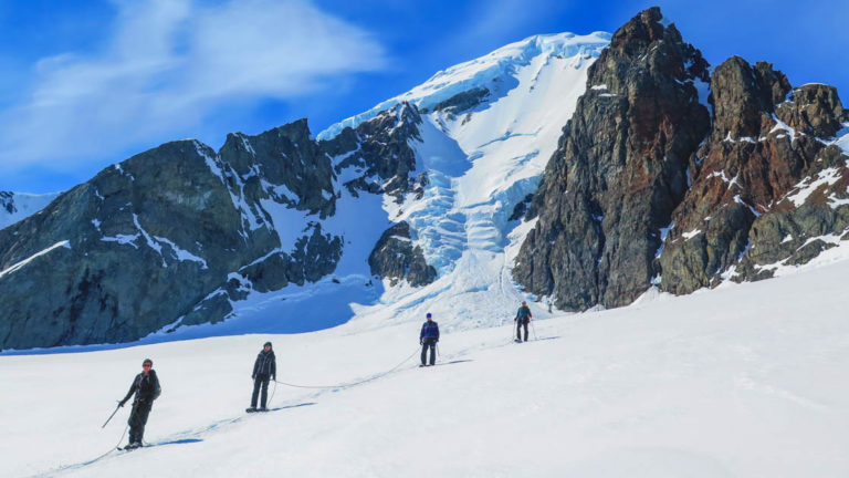 group of adventure travelers walks up a snowy mountain on a sunny day in antarctica
