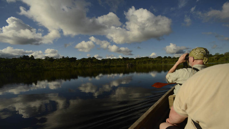 amazon travelers taking pictures from a small boat with the jungle in the distance on a sunny day with clouds above