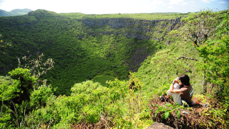 female solo traveler sits on the edge of a lush green galapagos valley and takes a picture