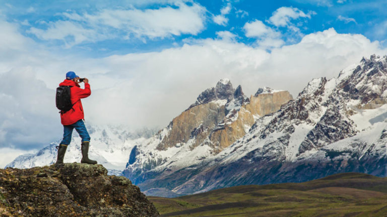 Hiker standing on rock and taking Photos of the snowy and jagged mountain landscape in Torres Del Paine National Park, Patagonia