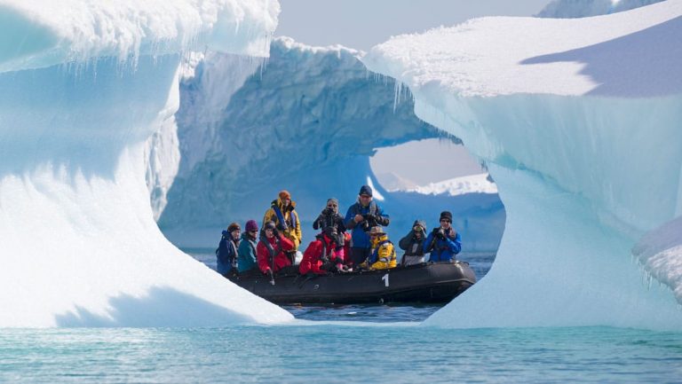 A zodiac full of guests from the antarctica air cruise passes in front of a pyramid shaped iceberg