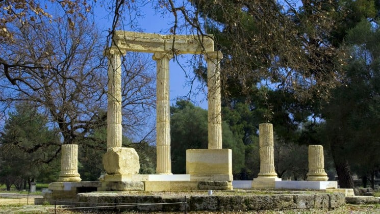 ancient greek columns standing in olympia with trees in the foreground