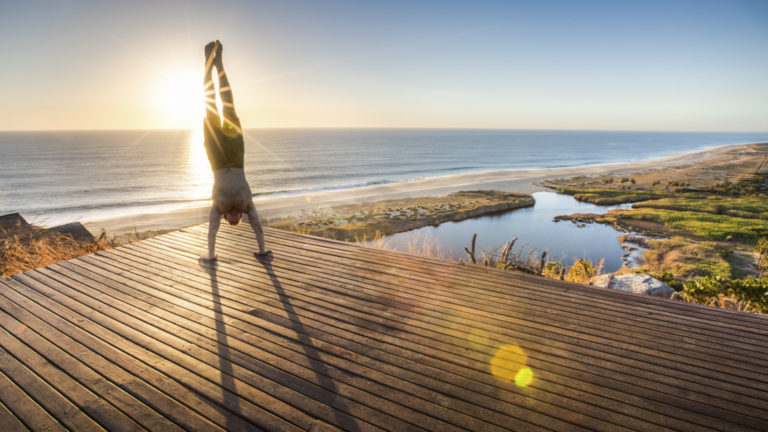 person doing a yoga hand stand on a platform above the beach during the sunset