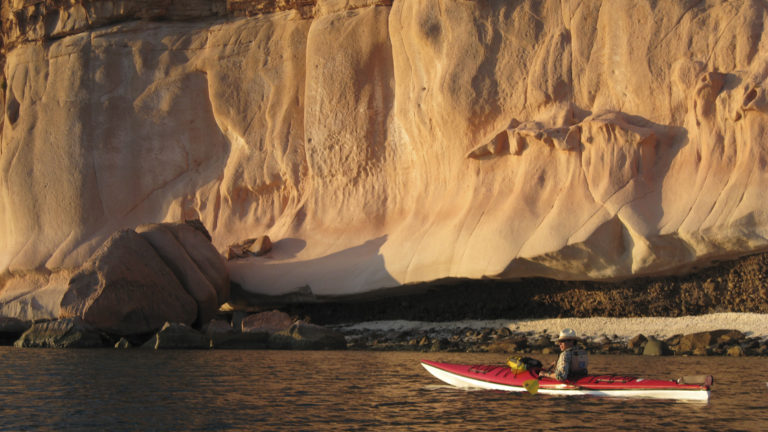 a kayaker paddling close the the uniquely shaped coastline cliffs of baja california