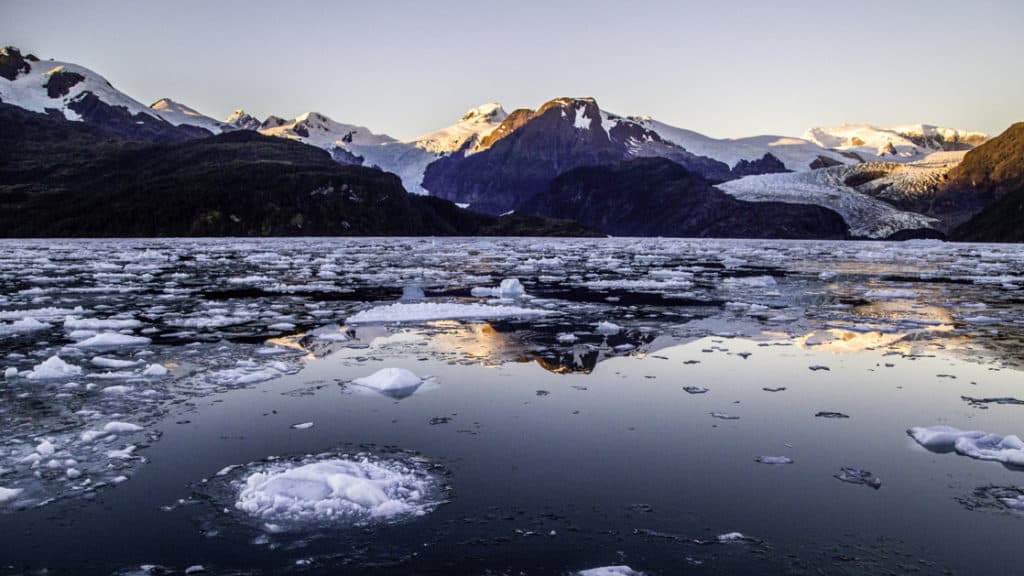 Ice on the calm and reflective water in front of a glacier in Tierra Del Fuego, Patagonia, during sunset