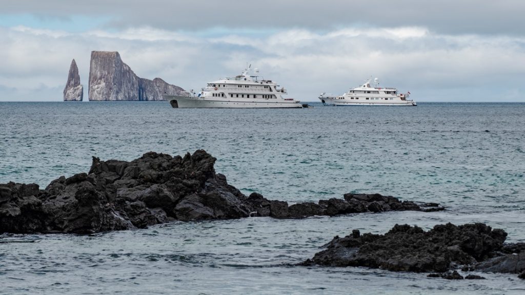 The all white Coral I and Coral II Galapagos cruise ships float on the horizon in front of Kicker Rock in the Galapagos Islands.