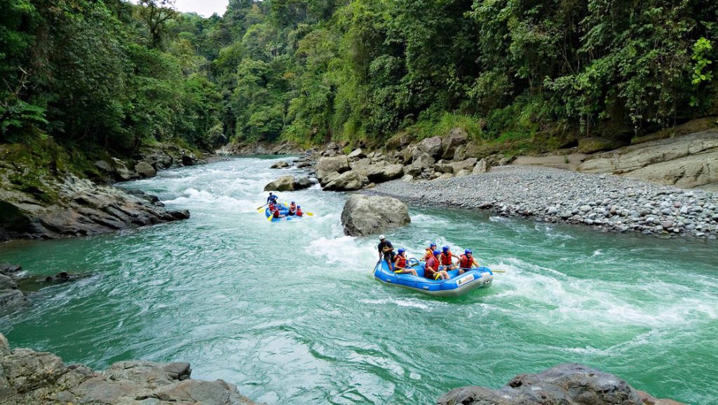 Two rafts of Costa Rica travelers floating down a turquoise river with rocks and green trees lining the river.