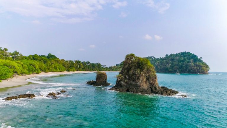Manuel Antonio beach in Costa Rica, with white sand, bright green forest, turquoise water & lots of sunshine.
