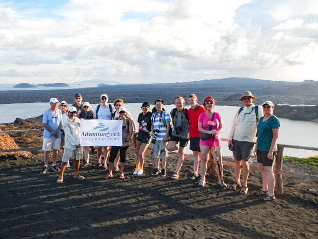 A small group of Galapagos travelers standing at an overlook holding an AdventureSmith flag