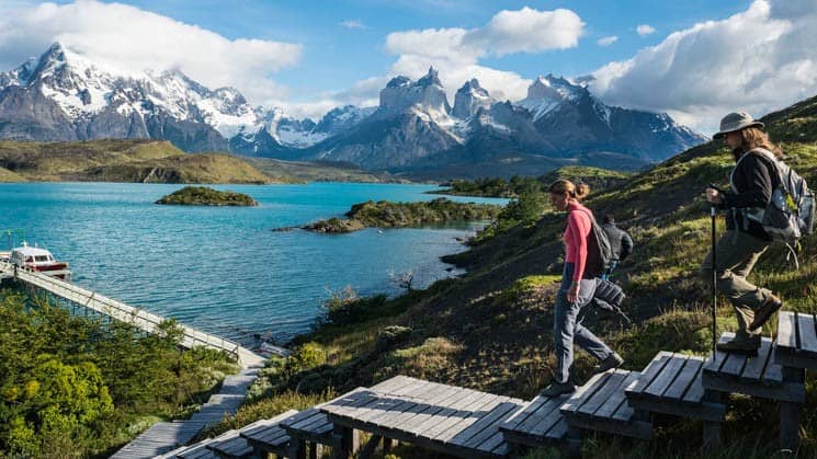 two trekkers walking down wooden steps to lake on explora patagonia land tour