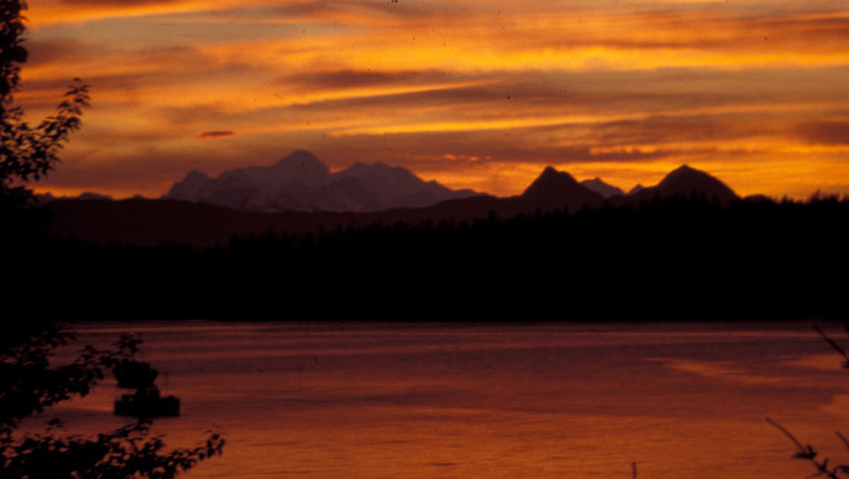 Orange sunset over the water with the silhouette of the fairweather mountains in southeast alaska