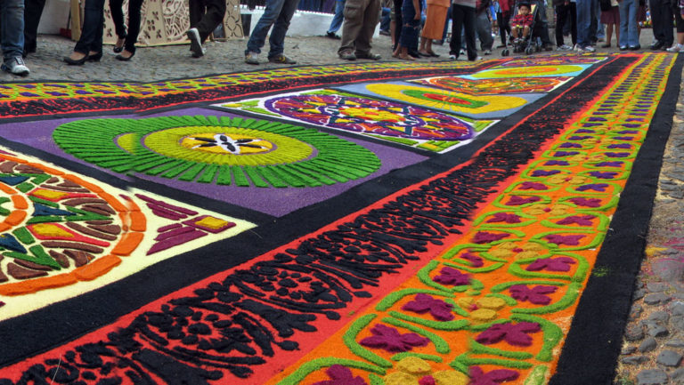 A colorful long Guatemalan carpet with many designs spread out on the street.