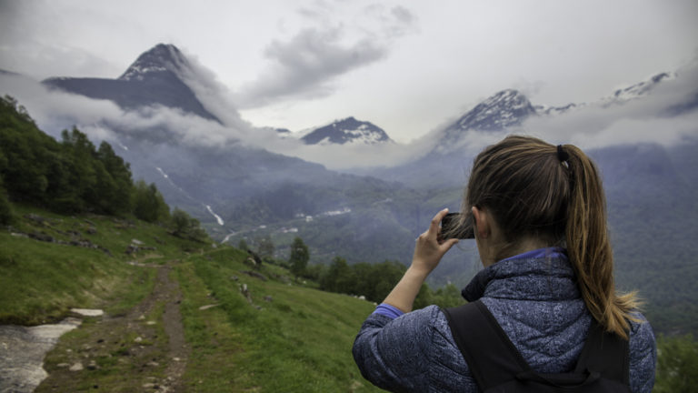 Woman taking a picture while on a hiking trail in Geiranger Fjord in Norway