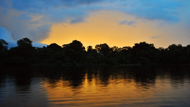 amazon river at night with the jungle reflecting off of the water and a cloud above