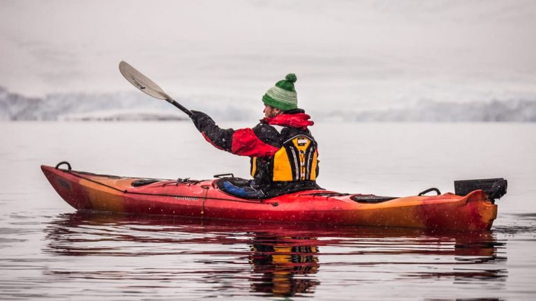Solo Kayaker in water paddling towards the snowy peninsula in the polar circle.