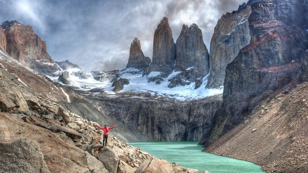 Hiker with arms up in the air in front of the green lake with the Cordillera del Paine mountains behind in Chile