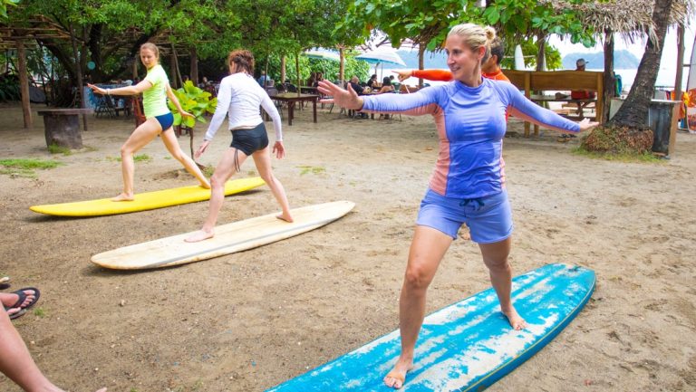 3 women stand on long surf boards during a surf lesson on the Manuel Antonio beach in Costa Rica.