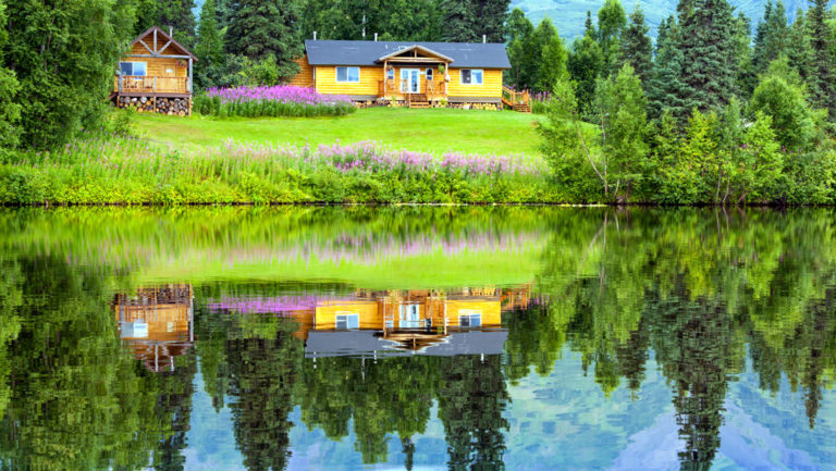 Winterlake lodge in the alaska range with a green lawn in front and a reflection in the still water