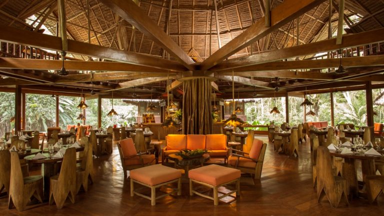 The dining room at Inkaterra Reserva is inspired by the tropical flavors of the Amazon region, with a tree trunk beam as the centerpiece, wood thatched roof and all wood carved tables and chairs.