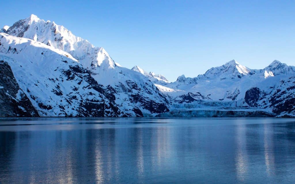 A snowy image of mountains and the John Hopkins Glacier reaching the bay as the sun sets on the mountain tops in Alaska's Glacier Bay National Park.