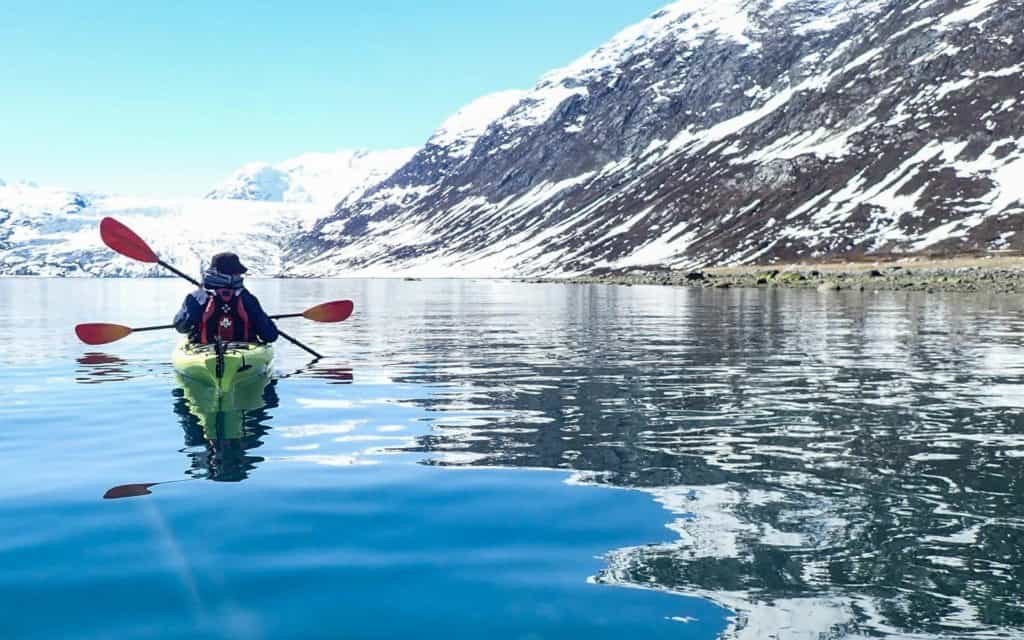 Two Alaska travelers kayaking in Glacier Bay National Park in Alaska on smooth waters in front of Reid Glacier.