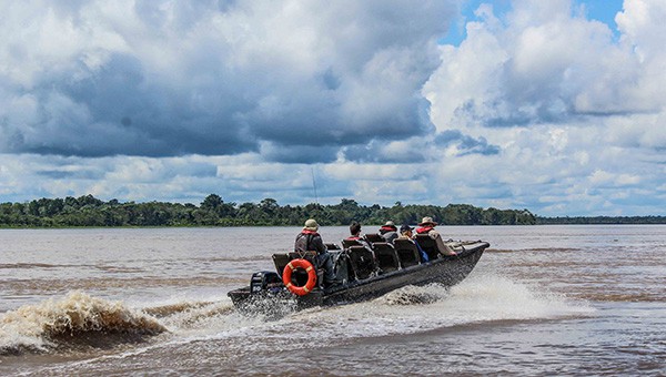 Amazon cruise travelers on a skiff tour in murky water on a cloudy day in the jungle.