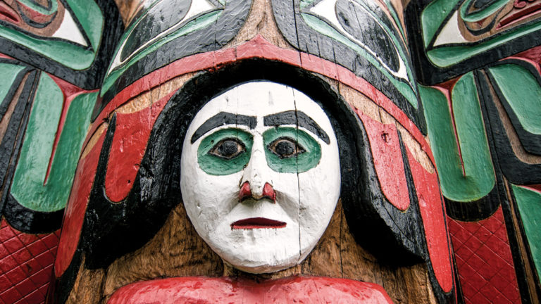 Close up on one section of a totem pole in Ketchikan Alaska, showing a white face with red and green accents.