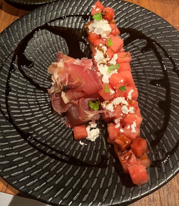 A black plate with pink watermelon salad and red fish served on Coral Adventurer small ship