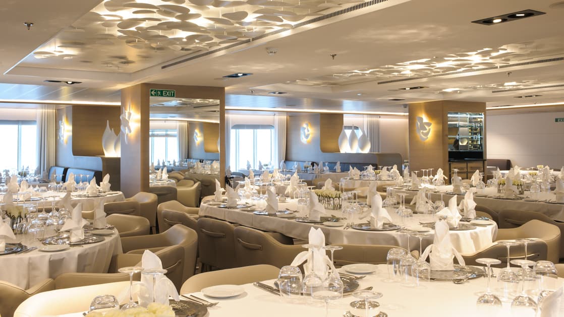 Gastronomic Restaurant aboard Le Soleal tan and white decor surround long rectangle and round tables the place mats are set with folded napkins