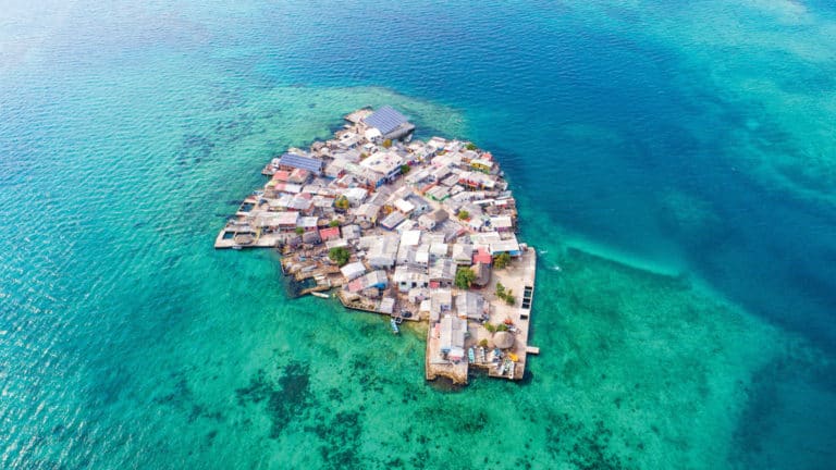 Aerial view of Santa Cruz del Islote, Colombia, a small island packed with buildings & surrounded by turquoise reef and brilliant blue waters.