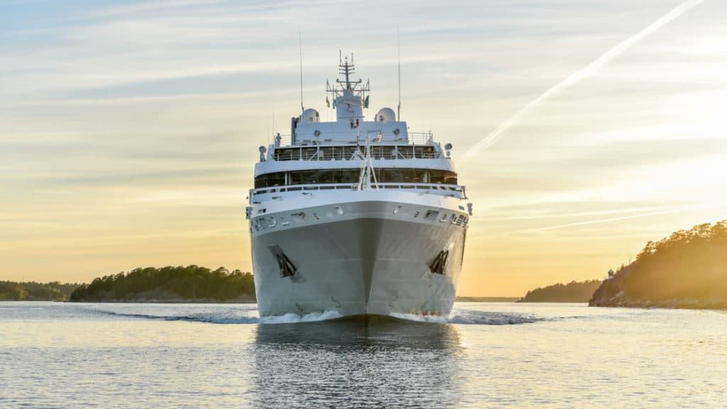 a peach sunrise sky is seen behind a frontal exterior view of the luxury expedition ship Le Soleal, she is mainly white with a light grey hull