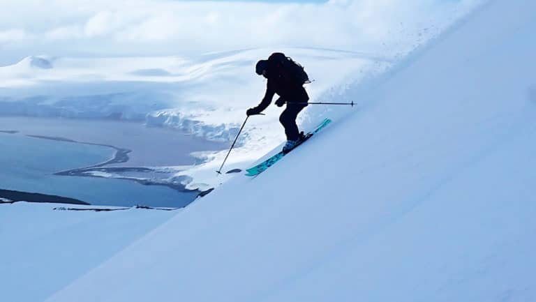 A backcountry skiier makes turns down a steep slope in Antarctica, on a cloudy day.