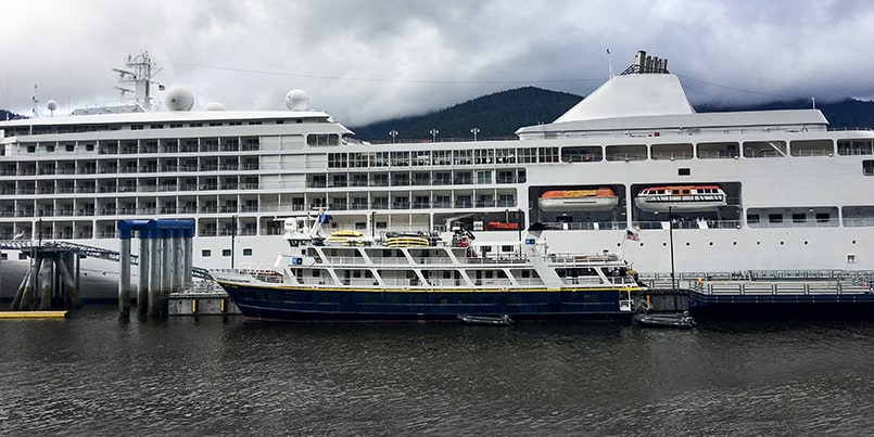 A small cruise ship seen directly in front of a larger big cruise ship.