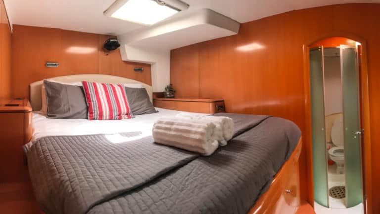 A cabin on Belize charter ship doris, glass door open to the restroom, a queen bed sits under a sky light in a room of wood walls